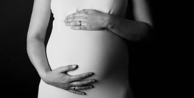 Pregnant woman in a white dress holding their belly.